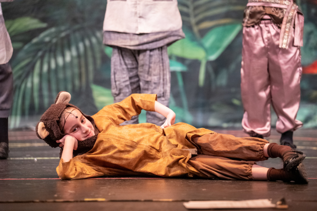 A cast member of Jungle Book Kids lying on the stage.